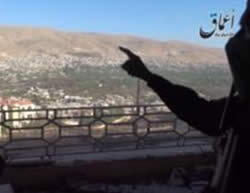 Armed ISIS operative pointing at the city and the mountain range overlooking it. 