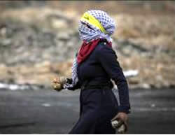 Une Palestinienne masquée ceinte d'un bandeau jaune du Fatah ramasse des pierres pour les lancer sur les forces de Tsahal au cours d'émeutes à Al-Bireh. 