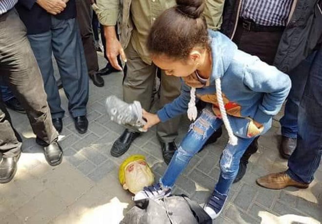 A girl stands on the neck of an effigy of Donald Trump and throws shoes at it during a demonstration in Nablus (Twitter account of QudsN, April 14, 2018).