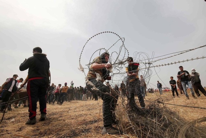 manifestantes palestinos tirando de la valla de alambre de púas y luego cortándola al este de Khan Yunis (Palinfo, 27 de abril de 2018).