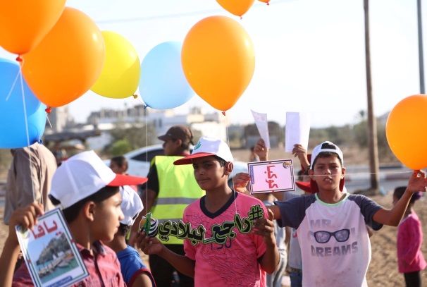 Launching balloons with the slogan of the summer camps and the names of cities and villages occupied by Israel in 1948. The boy at the left holds a notice with the word 