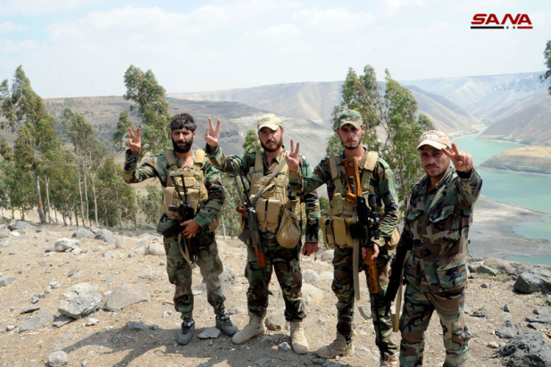 Des soldats de l'armée syrienne font le signe de la victoire avec le bassin du Yarmouk en arrière-plan.