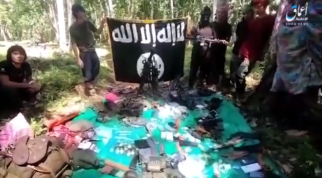 ISIS operatives next to the organization’s flag, along with weapons and equipment that had been seized (Amaq News Agency, November 19, 2018).