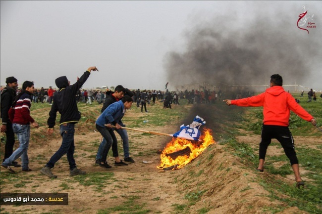 Des manifestants de la "marche du retour" brûlent des pneus et un drapeau israélien à Gaza (Page Facebook de l'Autorité nationale de la marche du retour, 15 février 2019)