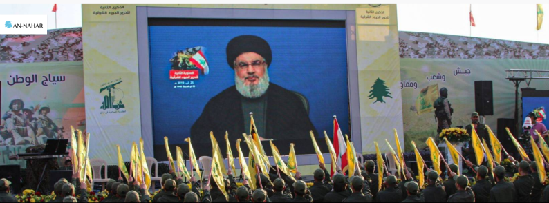 Operatives in uniform carrying Hezbollah and Lebanese flags cheer Nasrallah before his speech. 