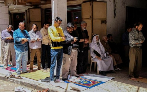 A group of vendors hold a public prayer on the sidewalk in a market (al-Majala, May 2, 2020).