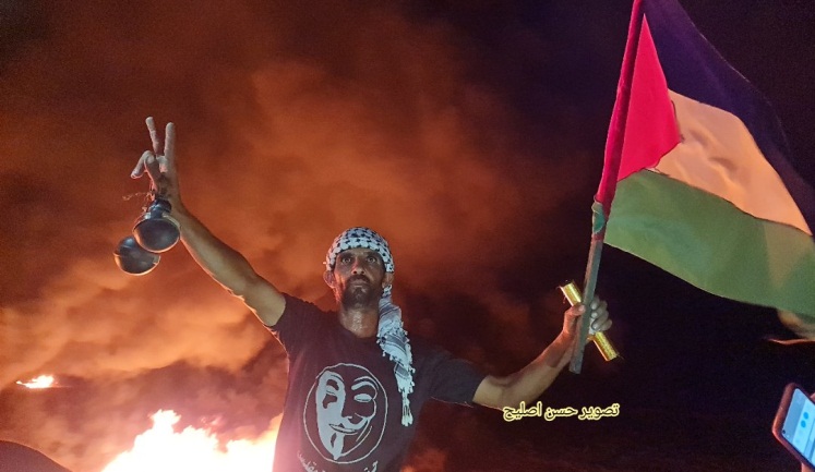 A Palestinian holds two hand grenades in one hand and a flag and a pipe bomb in the other (Twitter account of journalist Hassan Aslih, August 30, 2021).