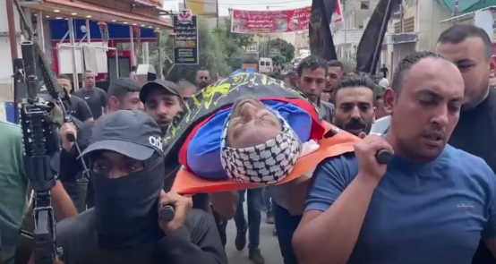 Amjad 'Aref Jass's body, wrapped for burial in a PIJ flag (Shehab, June 20, 2023).