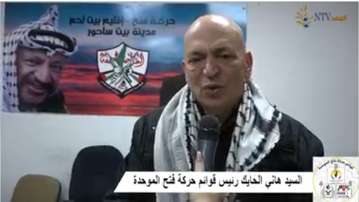 Hani al-Hayek during the 2022 election campaign, interviewed with a Fatah poster in Beit Sahour. The caption under his name reads, "Hani al-Hayek, head of Fatah's United Lists (al-Mahed TV Facebook page, March 24, 2022)